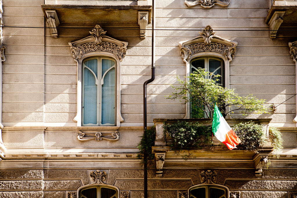 European stone building with large windows and an Italian flag on the balcony